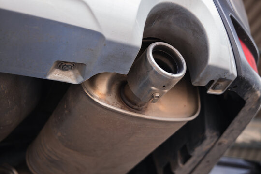 Close up of a car exhaust pipe and muffler viewed from the undercarriage. Automotive emissions system inspection and vehicle maintenance in an auto repair garage