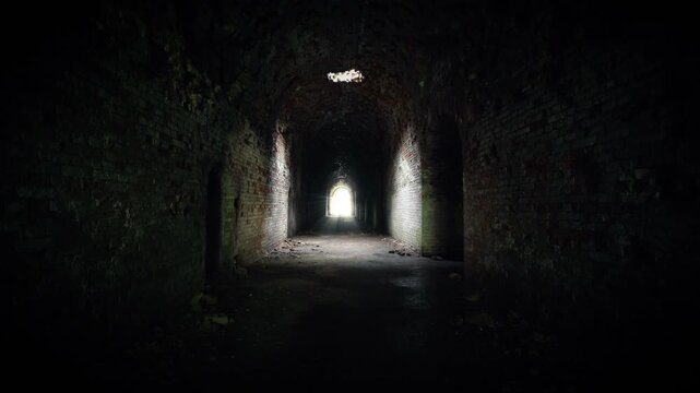 Dark abandoned brick tunnel interior with arched walls and scattered debris, leading toward a bright opening as the camera slowly advances through the corridor