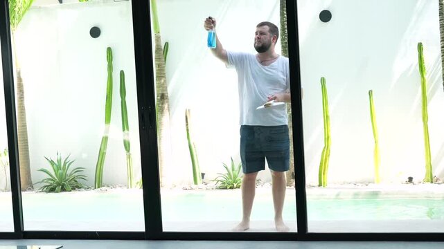 Man cleans large exterior glass windows of a modern house using professional window cleaning tools. Outdoor residential window washing and home maintenance.
