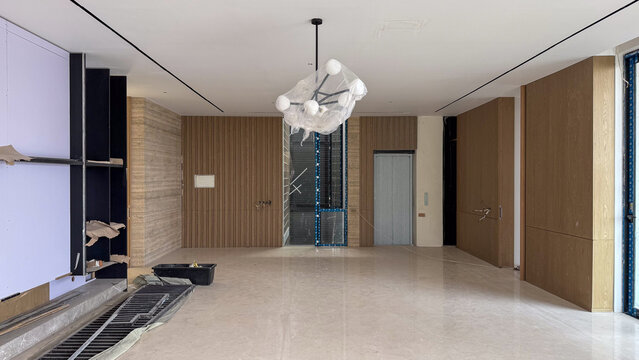 Spacious living room with polished shiny marble flooring a modern chandelier wrapped in plastic and minimalist wooden decorative wall panels.