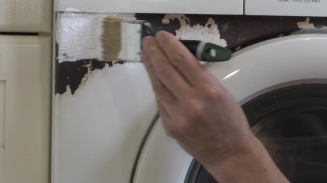 painting a washing machine from rust, A man paints a rusty washing machine with white paint using a brush