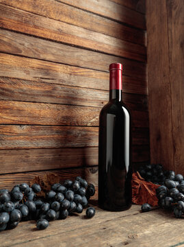 Red wine bottle with blue grapes on an old wooden table.