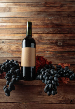 Red wine bottle with blue grapes on an old wooden table.