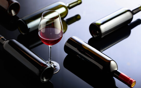 Glass and bottles of red wine on a black reflective background.