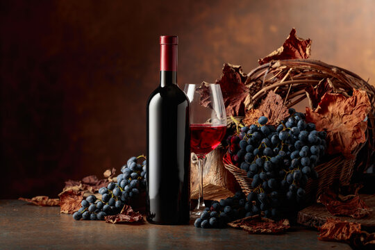 Bottle of red wine with blue grapes on a brown background.