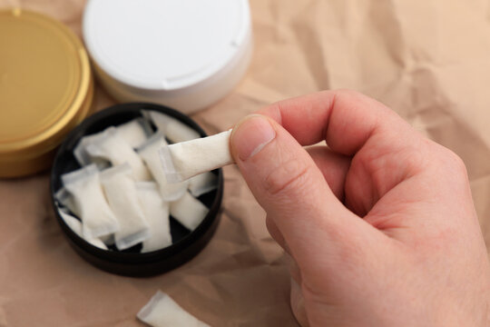 Hand holding snus pouch over open can in indoor setting during daytime