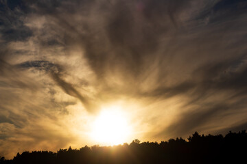 Fototapeta premium Golden sunbeams breaking through dramatic, swirling storm clouds above a dark forest silhouette, creating a divine and moody celestial display of natural beauty during late afternoon golden hour