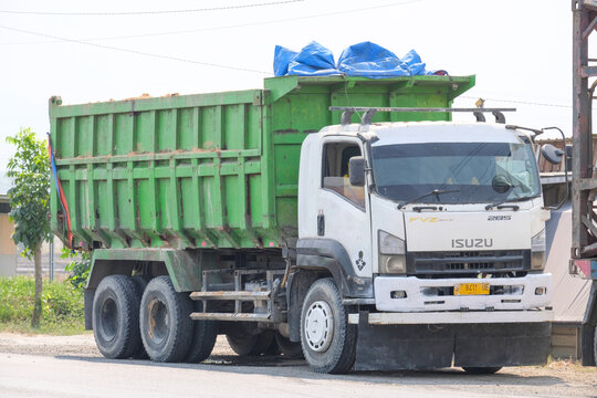 An Isuzu FVZ 285 dump truck with a large green cargo bed parked on the side of a dusty road under bright daylight.