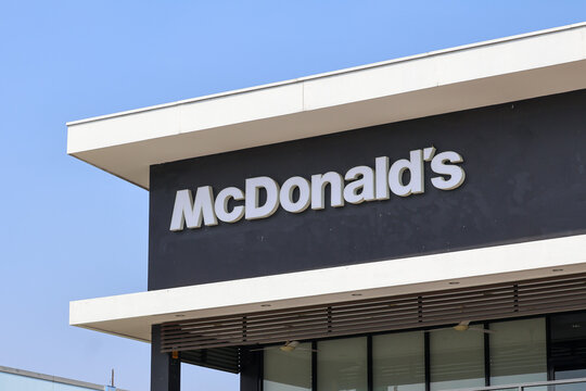 A close-up shot of the white McDonald's brand signage attached to a modern dark grey and white building facade against a clear blue sky background.