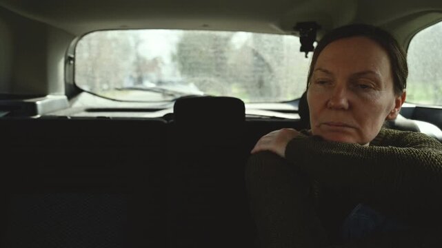 Thoughtful middle-aged woman sitting in back seat of car looking out window, quiet reflective travel moment, 4K