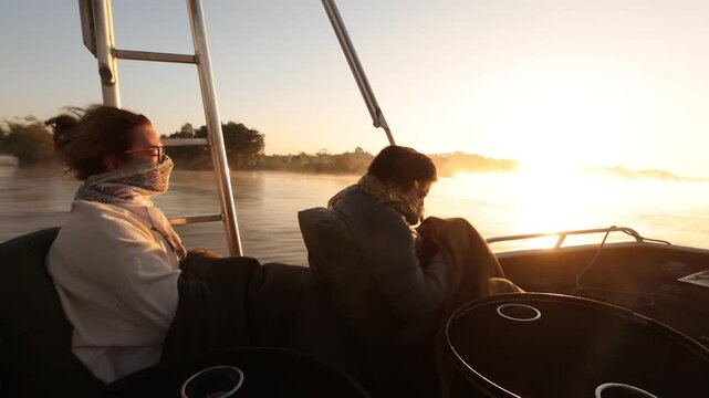 young woman and younger brother traveling on speedy boat  at sunrise on the mighty Zambezi River, Zimbabwe, Africa...mist rising on water