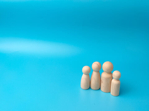 Four simple, blank wooden peg dolls of varying heights stand grouped together in a line against a blue background