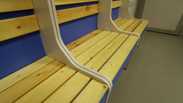 Neatly polished wooden planks of empty dressing area seating stalls. Tidy minimalist construction suggests order and quality in locker room