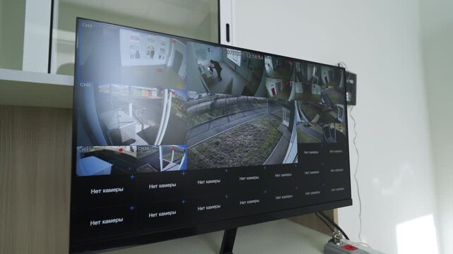 Large widescreen display sits on office table showing remote observation application. Organized layout suggests professional security