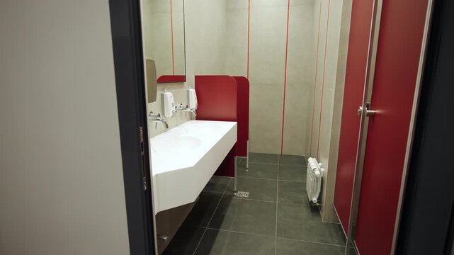 Open doorway reveals clean public restroom with bright red toilet cubicles. Modern tile design creates neat functional environment