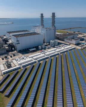 Aerial view of the Maxima Power Plant featuring rows of solar panels and industrial chimneys on the coast of the Markermeer in Lelystad, Flevoland, The Netherlands.