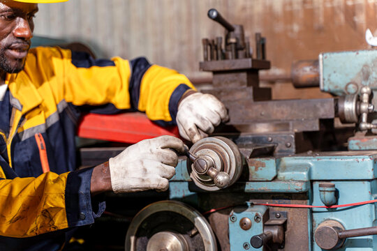Closeup and clop black male industrial engineer in uniform checking old model lathe and drilling machine at industrial workshop.