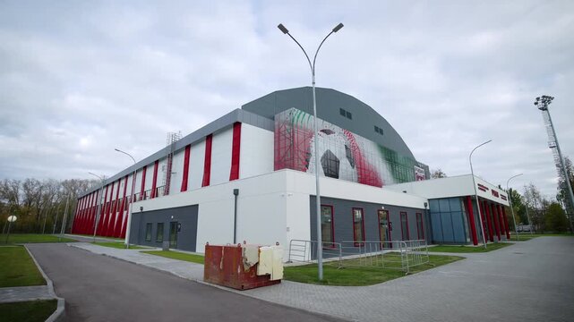 Exterior of modern massive football arena under cloudy sky. Large soccer ball graphic decorates side facade wall supporting sports themes