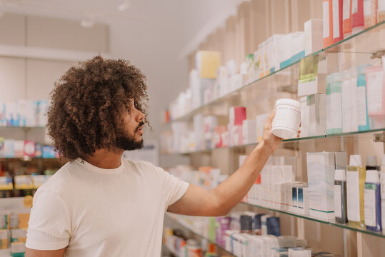 Young man with afro hair choosing skincare product from drugstore shelf