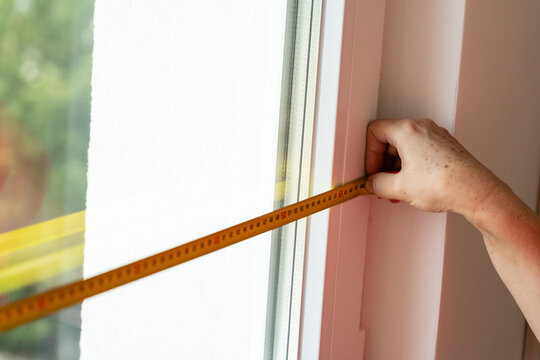 Person measuring white window frame with a yellow tape measure