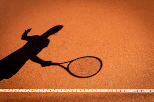 Schatten eines Tennisspielers mit Tennisschl&auml;ger auf einem Sandplatz als kreatives Symbol f&uuml;r Tennissport, Bewegung und Wettkampf.