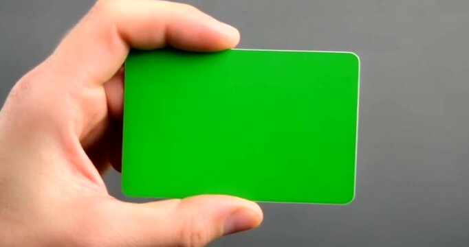 Hand holding small bright green screen rectangle card against gray background for compositing.