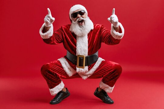 Full length photo of handsome old dabber fat funny santa claus in eyeglasses dance with his hand raised in a funny pose, isolated over red background