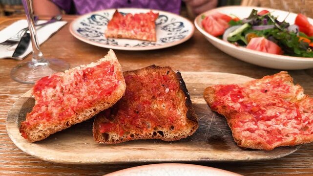 Close-up of a hand picking up a slice of traditional Spanish pan con tomate from a serving plate. Authentic Mediterranean tapas with toasted rustic bread, fresh tomato and olive oil. High quality 4k