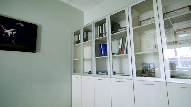 Administrative office features cabinets with glass display doors holding binders and folders. Picture of football player hangs on wall