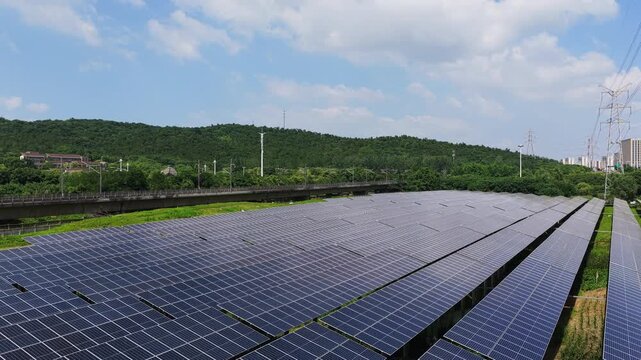 Aerial view of solar panels beside railway and green hills
