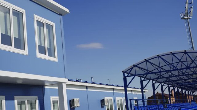 Glass windows with plastic frames line facade of functional sports building. Daytime sky creates calm background for modular architecture