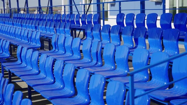 Plastic seats line outdoor stadium tribune under matching metal canopy frame. Clean empty seating section stands ready for spectators