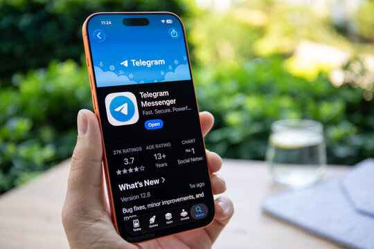 Man hands holding phone Apple iPhone 17 Pro Max in Cosmic Orange at the table, displaying application Telegram on screen App Store