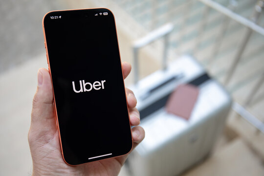 Man hands holding phone Apple iPhone 17 Pro Max in Cosmic Orange outdoors on suitcase and passport holder, displaying Uber ride sharing app taxi on the screen