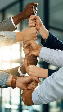 Diverse hands stacked in a fist bump tower symbolizing unity and teamwork against a blurred background of light and glass