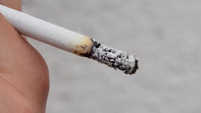 Macro shot of hand holding a smoldering cigarette with ash