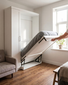 Hand lowering murphy wall bed halfway out of cabinet in compact flat