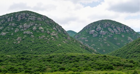 Obraz premium Beautiful landacape view of large green rocky hills against light cloudy sky 
