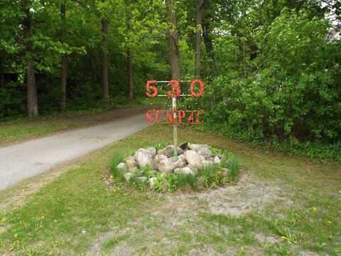 A red metal sign displaying 530 SUNPAC stands proudly above a small roche garden near a pathway, creating a joli site.