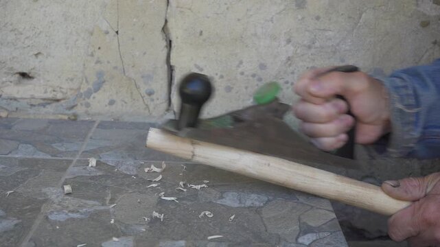 A man plans a wooden stick with an old metal plane, Carpenter working with hand plane shaving wood chips off a wooden stick