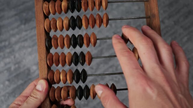 Male hands carefully slide the beads of a vintage wooden abacus over a gray textured background. Concept of traditional accounting, ancient mathematics, and historical business calculation.