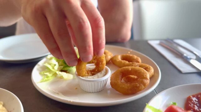close up of person dipping breaded calamari ring in dipping sauce at restaurant