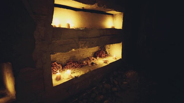 Candlelit stone niche memorial glow, warm amber light pooling over wax, scattered petals and moss, sootstreaked masonry and quiet rubble evoke reverence