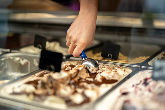 Hand scoops vanilla chocolate swirl from cold freezer