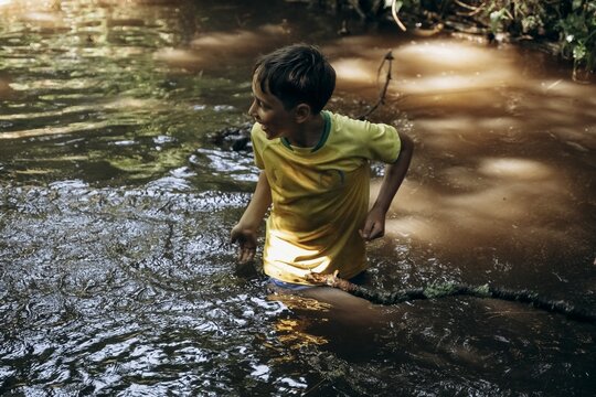 Child enjoying a summer day exploring a muddy stream, showing curiosity and excitement. The scene captures youthful adventure, nature interaction, and playful exploration.