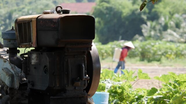 Old farm machine at the edge of a green field with a farmer working in the background. Rural livelihood.