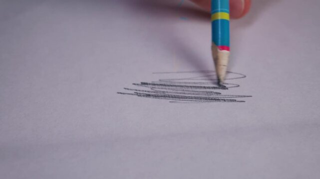 A close-up view shows a hand sketching grey lines on a smooth white surface. The blue pencil tip leaves traces of graphite that shimmer under light. These marks represent carbon science.