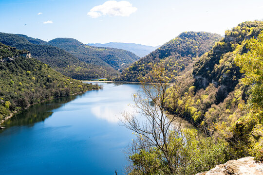 Panoramic view of Sant Pere de Casserres Benedictine monastery overlooking the Sau Reservoir and Ter River meander in Catalonia, Spain, surrounded by forests and mountains.