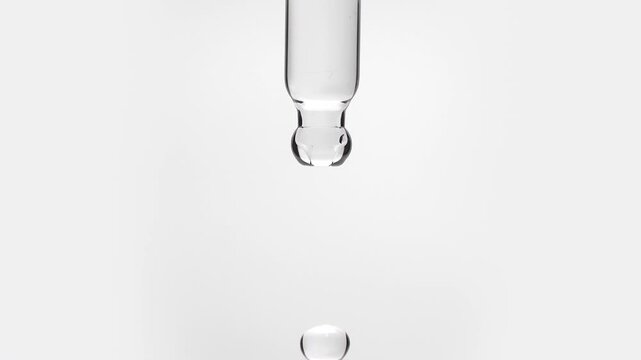 Macro shot of a pure micellar water or transparent salicylic acid serum droplet falling from a glass pipette dropper in slow motion isolated on a solid white background