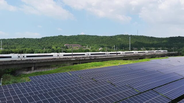 High-speed train beside solar panels and forested hills